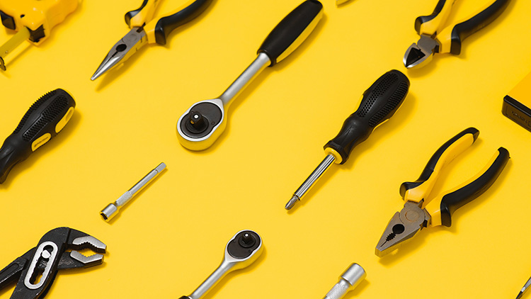 Image of various hand tools, including pliers, screwdrivers, wrenches, and ratchets, arranged on a bright yellow background. The tools are organized in a pattern, highlighting a variety of equipment used for mechanical and technical tasks.